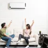 Couple enjoying comfort at home using remote to control air conditioner above beige couch in modern living room.
