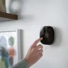 Person adjusting a modern black smart thermostat displaying 72 degrees mounted on a white wall.