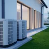 Two outdoor air conditioning units installed beside a modern house with large windows and green lawn.