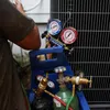 HVAC technician checking refrigerant pressure gauges connected to an air conditioning unit outdoors