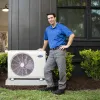 Technician standing next to a Carrier air conditioning unit outside a modern home with greenery.