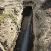 Trench in the ground with a black PVC pipe installed for underground utility or drainage work