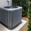 Outdoor central air conditioning unit installed on concrete slab beside house wall and green bushes.