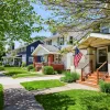 Row of suburban houses with front porches, green lawns, and an American flag on a sunny day.