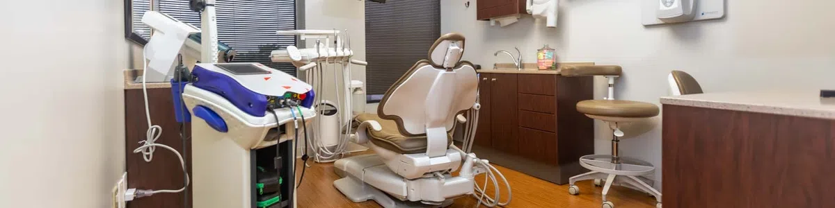 Modern dental clinic room with beige dental chair, equipment, monitor, and wood flooring under bright lights