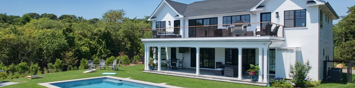 Modern white house with a swimming pool, lounge chairs, and lush greenery under a clear blue sky.