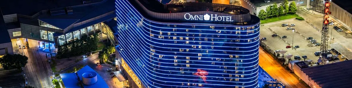 Night aerial view of Omni Hotel illuminated with blue lights and surrounding city street and parking lots.