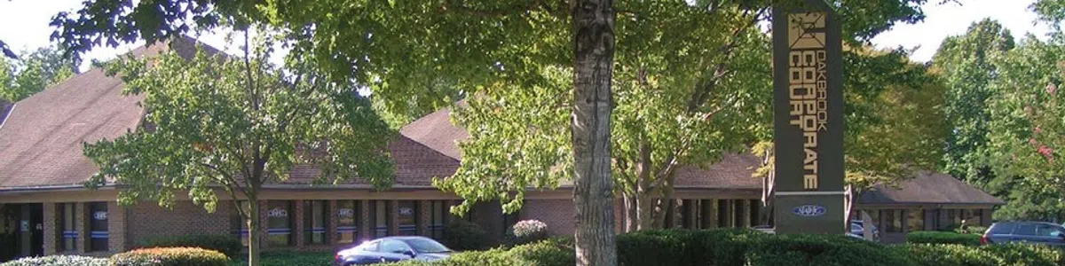Office building with brown roof surrounded by trees and bushes with a corporate court sign in front