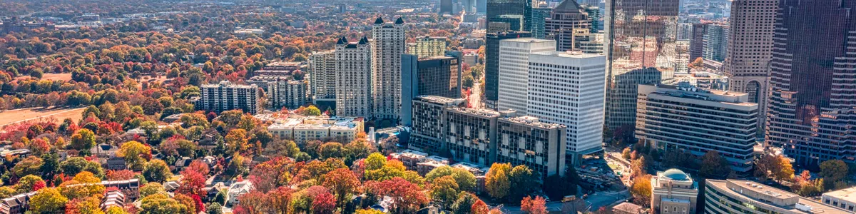 Aerial view of a city skyline with autumn trees showing vibrant red, orange, and green foliage under a clear blue sky.