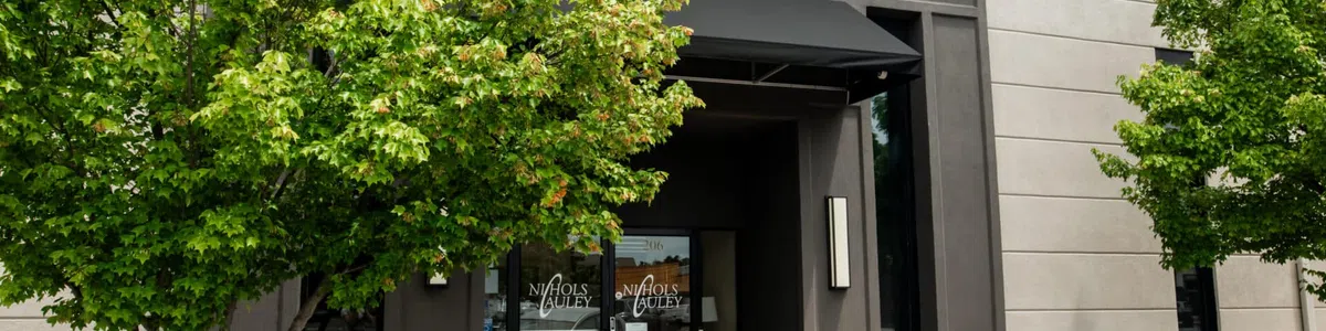 Stylish building entrance with dark framed glass doors, green trees, and a parked silver car outside.