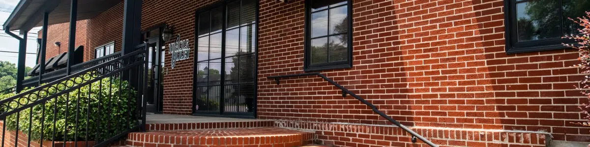 Curved brick steps leading to a black awning entrance on a red brick building with metal railings and plants.