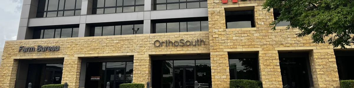 Front view of a multi-story office building with stone and glass facade under a cloudy sky.