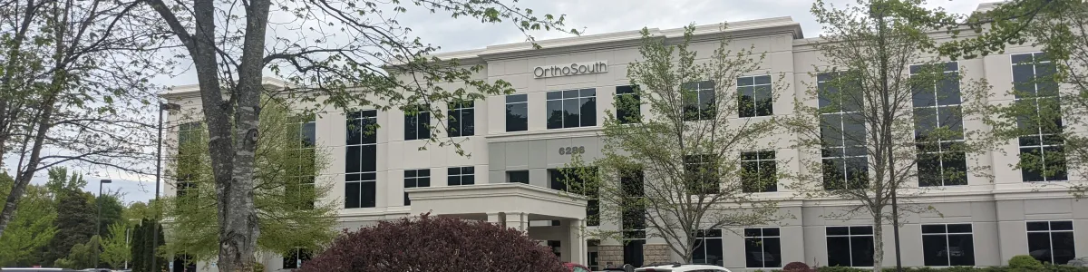 Modern three-story OrthoSouth medical office building with trees and parked cars on an overcast day