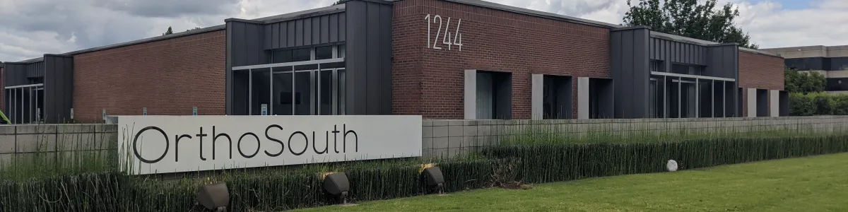 OrthoSouth medical office building with brick facade, large windows, and a green lawn under a cloudy sky.
