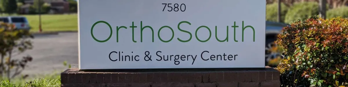 OrthoSouth Clinic & Surgery Center sign with flowers and greenery in a sunny outdoor setting.