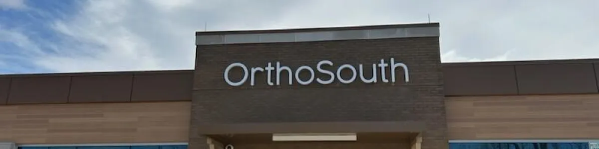 Exterior view of OrthoSouth medical clinic entrance with glass doors and clear sky above.