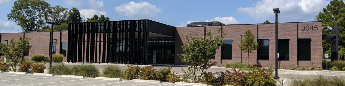 Modern single-story office building with brick facade and black glass entrance under a blue sky.