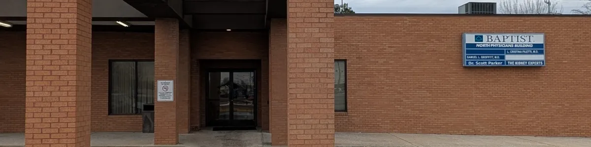 Entrance of a brick medical office building with covered walkway and handicap parking spaces under cloudy sky.