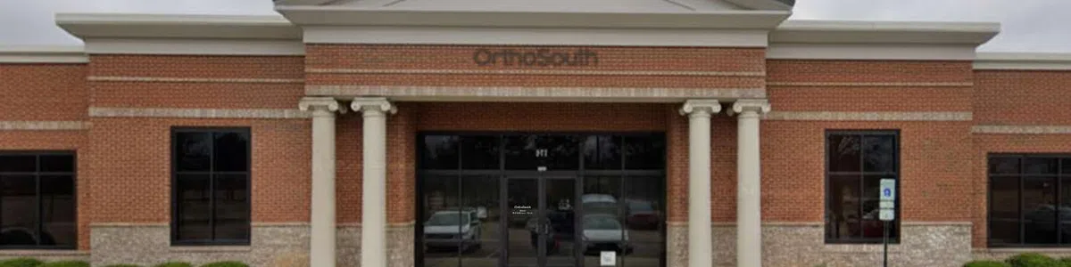 Exterior view of a brick commercial building with columns and glass entrance under a cloudy sky.