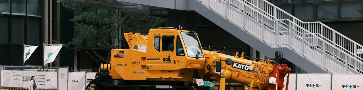 Yellow mobile crane at an urban construction site with traffic cones and safety barriers around it.