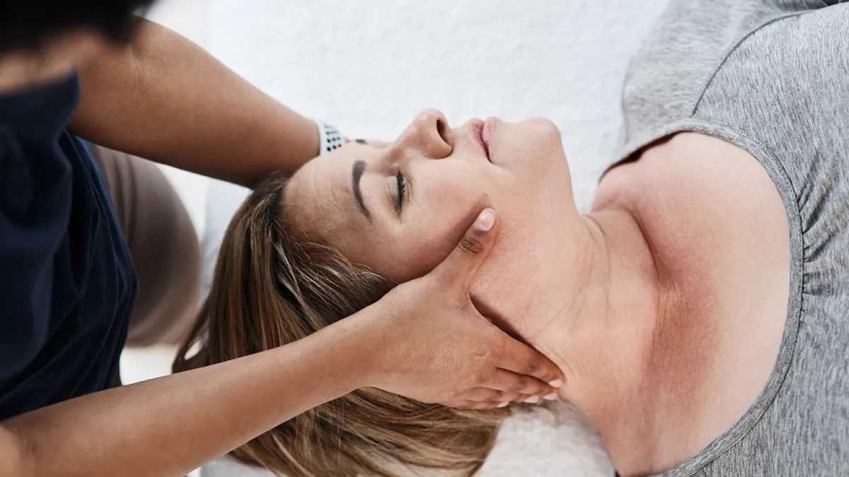 Woman receiving a relaxing neck and face massage while lying on a white towel.