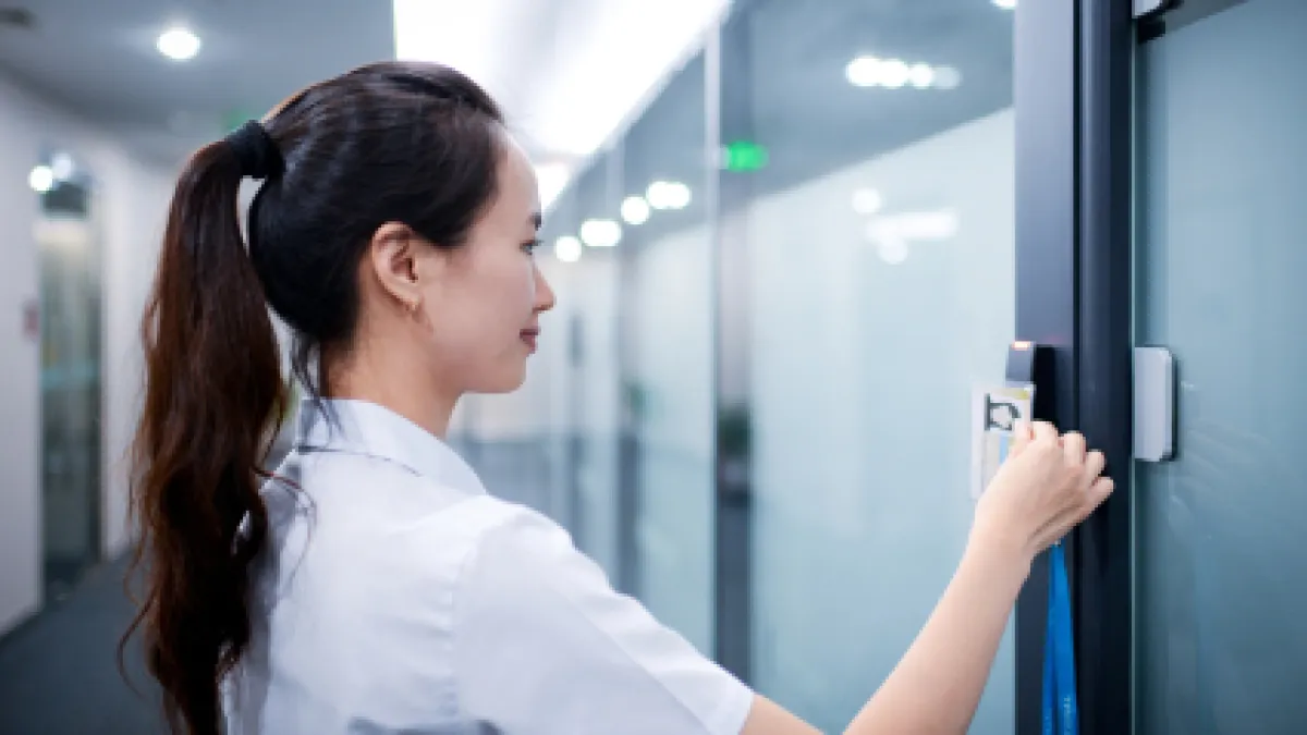 Woman in white shirt using key card to access office building door in modern hallway.