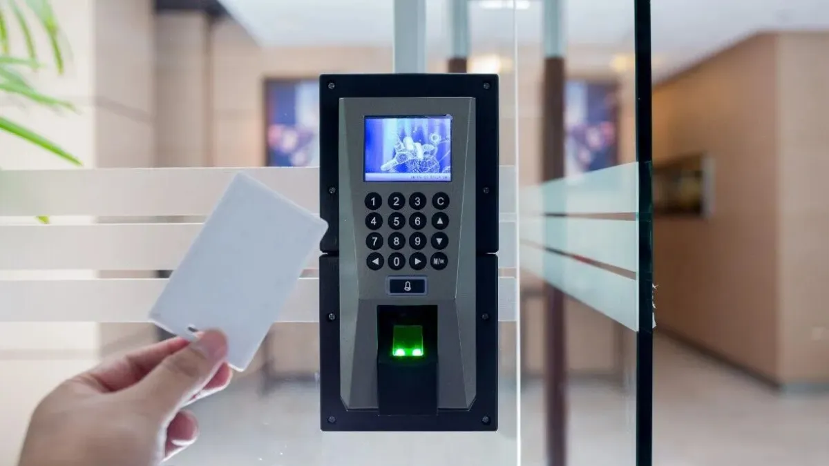 Hand holding RFID access card near electronic keypad and fingerprint scanner