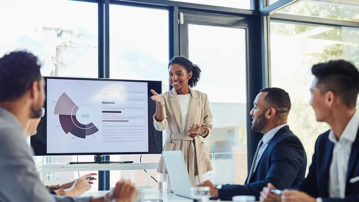 Businesswoman presenting sales data to colleagues in a modern office meeting with charts on screen.