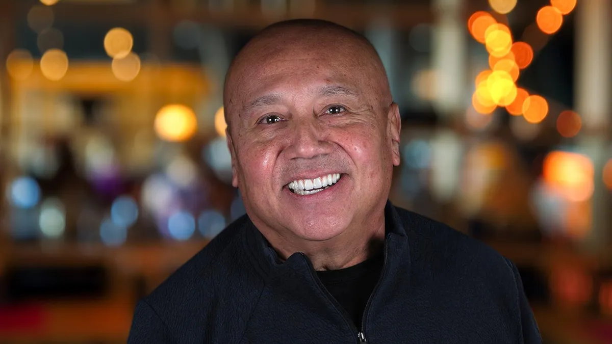 Smiling man with a warm expression, blurred lights in the background create a vibrant atmosphere.