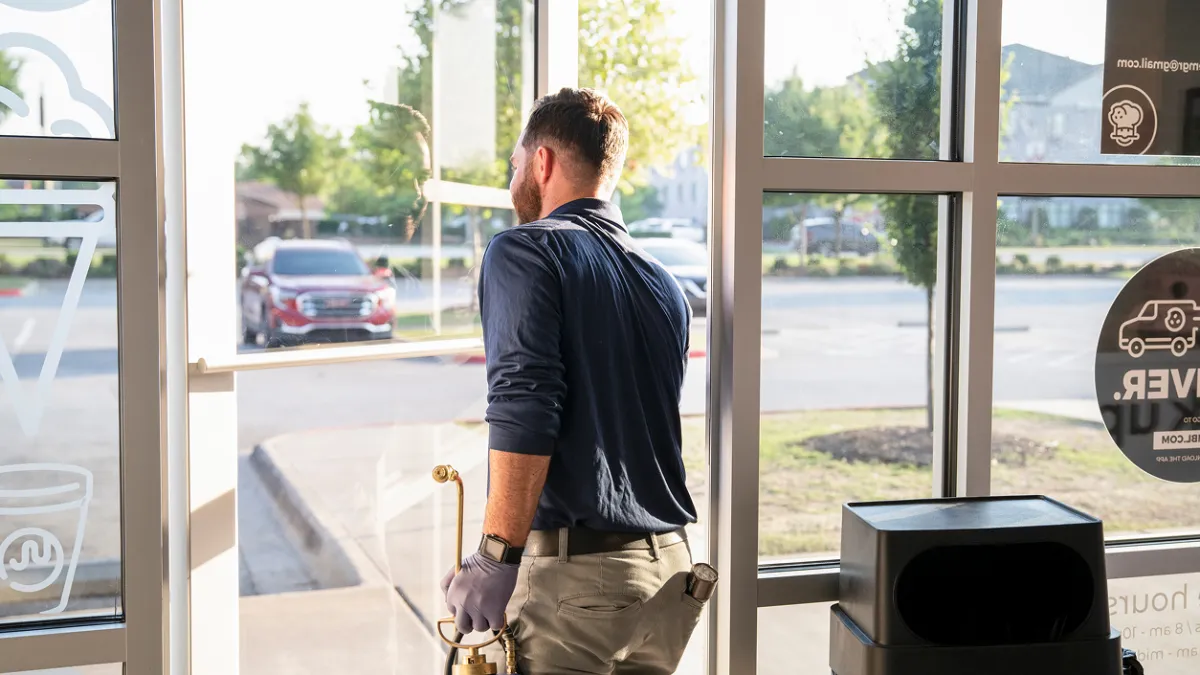 Man cleaning glass door with tools in bright, modern storefront environment.