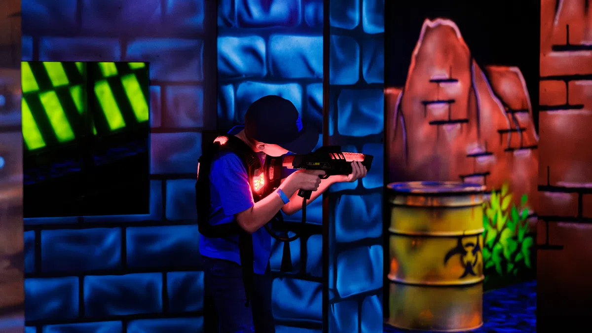 Child playing laser tag indoors with neon blue and orange lights in a futuristic arena environment.