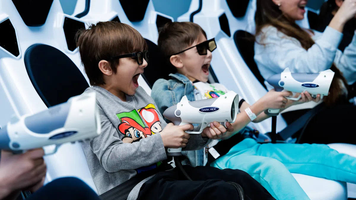 Children wearing 3D glasses and holding toy guns enjoy an interactive arcade shooting game.
