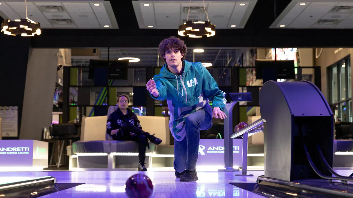 A young bowler in a green hoodie prepares to roll a bowling ball down the lane at an entertainment center.