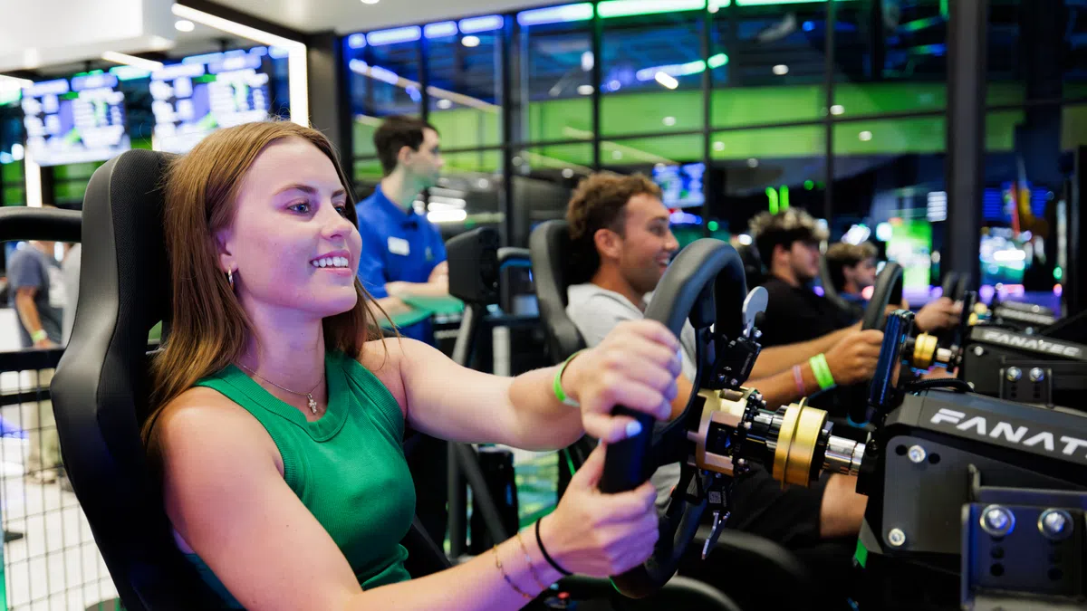 Young woman enjoying a racing simulator game with others in a bright, modern arcade setting