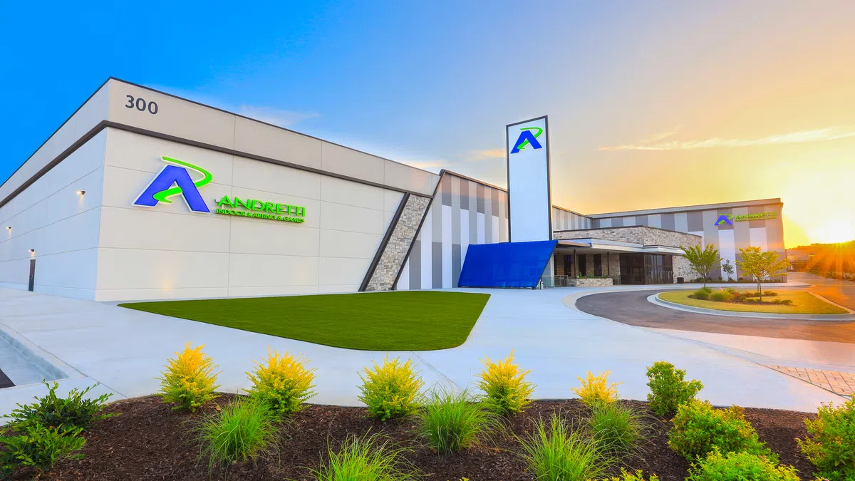 Modern Andretti motorsports facility building with a landscaped lawn under a blue sky at sunset.