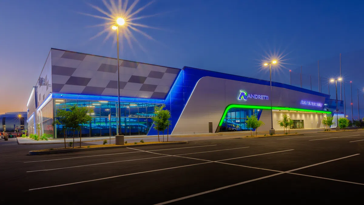 Modern Andretti racing and entertainment center illuminated at dusk with blue and green LED lights.