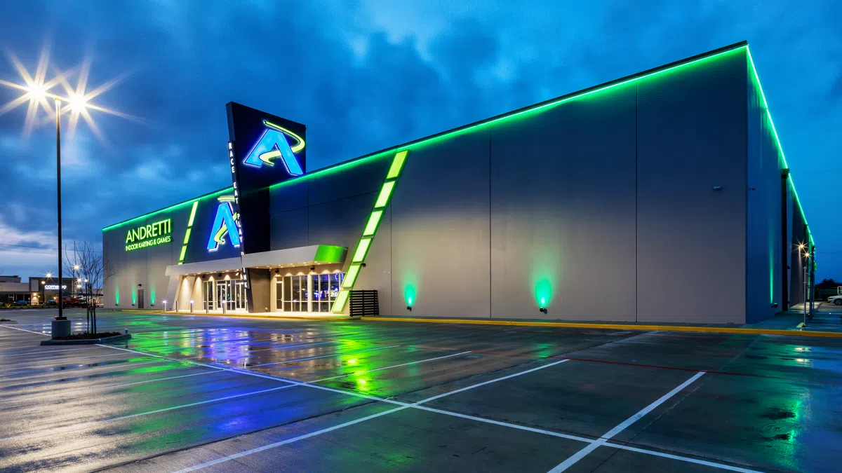 Andretti Indoor Karting and Games building illuminated with green and blue lights at dusk with empty parking lot.
