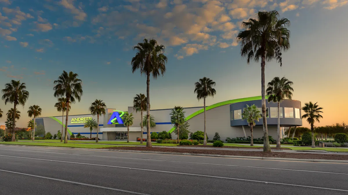 Andretti Indoor Karting & Games building with palm trees at sunset and clear partly cloudy sky.