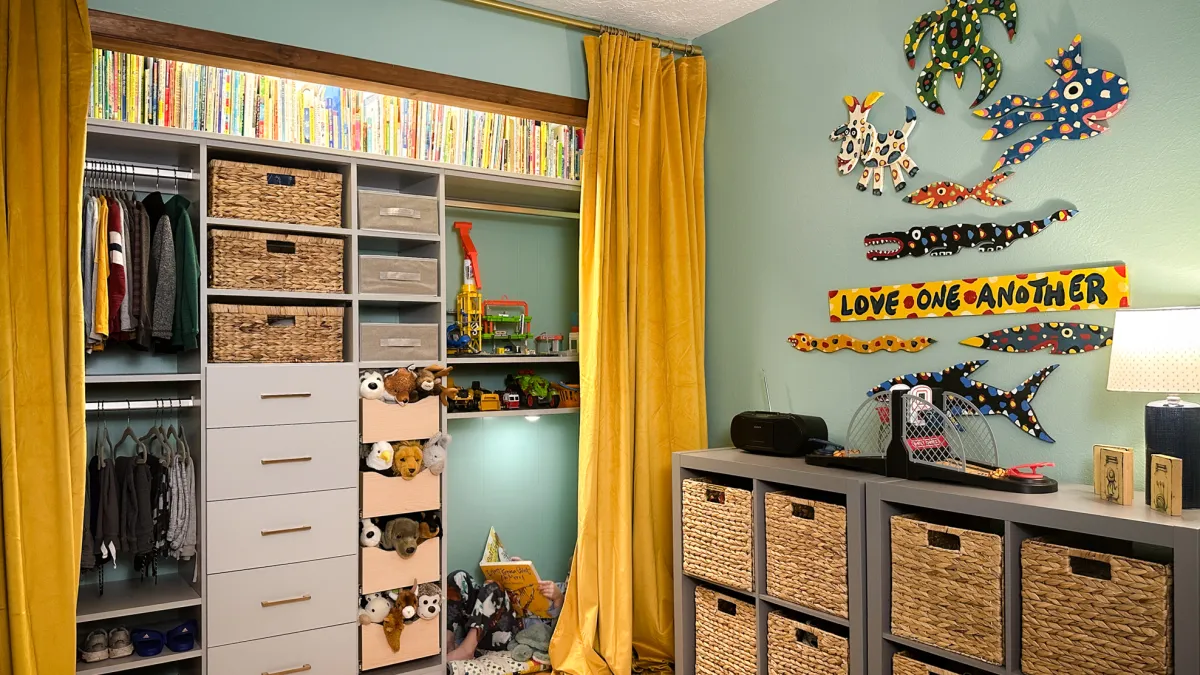 a childrens reach in closet with tan drawers, shelves with wicker baskets, books, toys, shoes, hanging clothing and cubby holes with wicker baskets