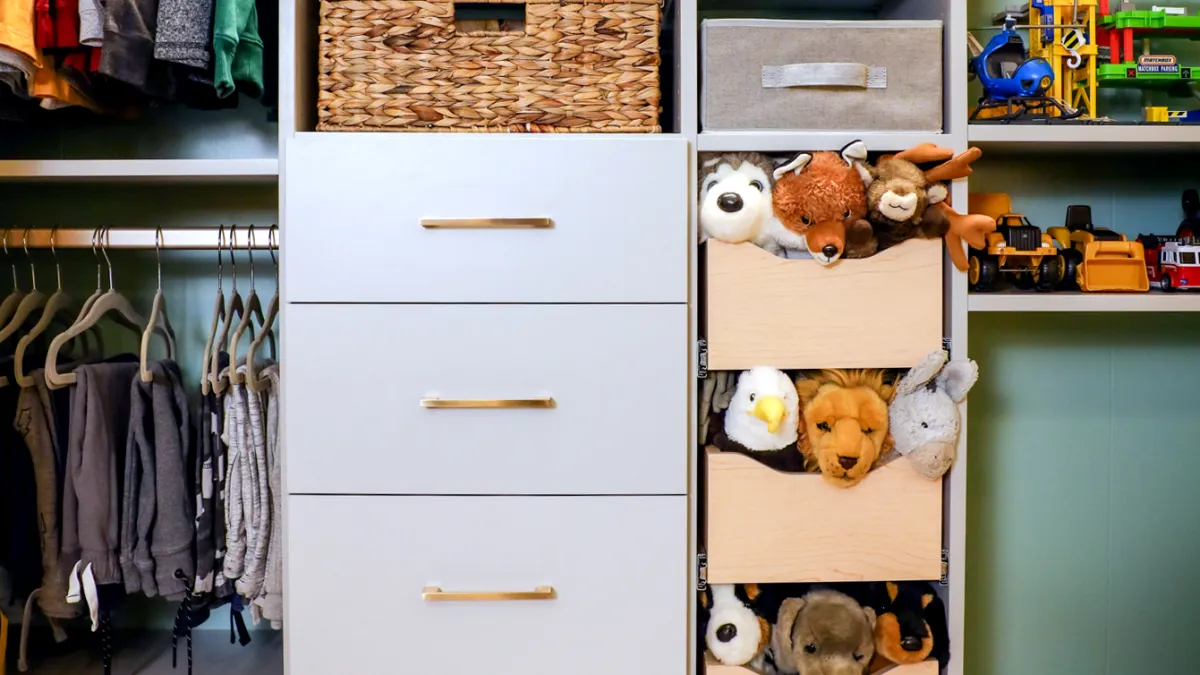 childrens reach in closet with white drawers and shelves, wicker baskets, toys, stuffed animals, shoes and hanging clothes