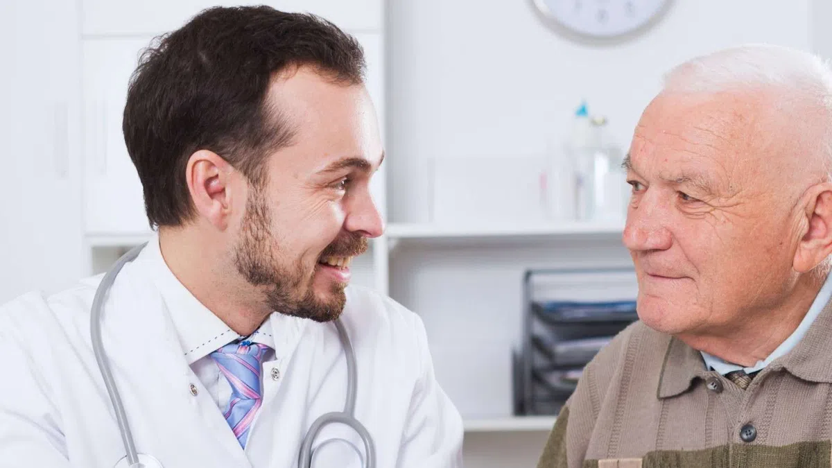 Doctor consulting with elderly male patient in medical office, discussing health documents and treatment plan.