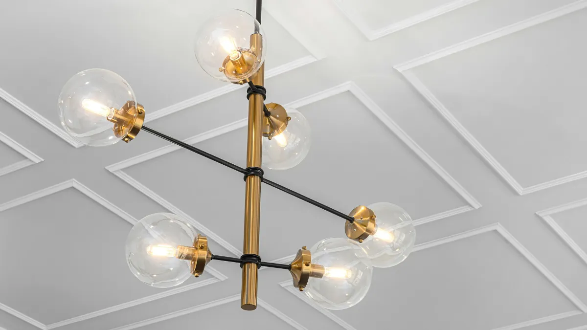 Modern chandelier with six exposed bulbs and brass accents hanging from a white decorative ceiling.