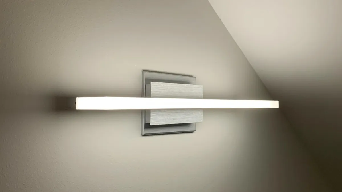Modern LED wall light fixture with sleek horizontal bar design illuminating a beige wall under a sloped ceiling.