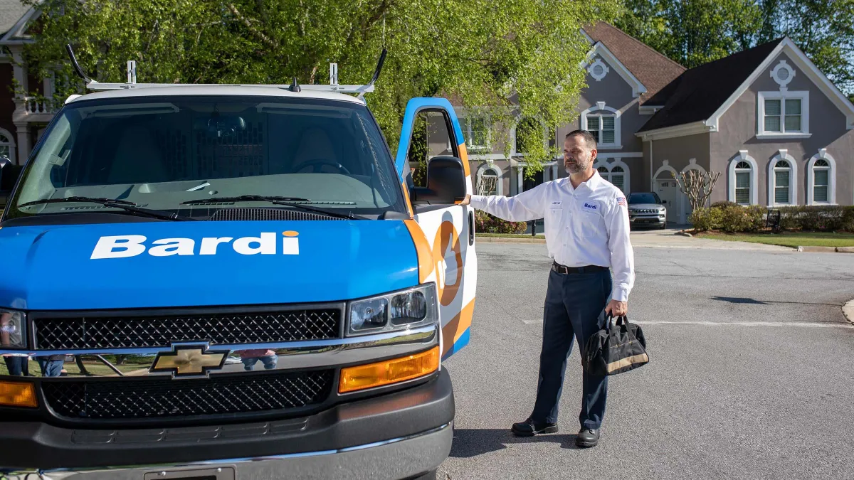 Technician standing by a branded service van in a residential area on a sunny day.