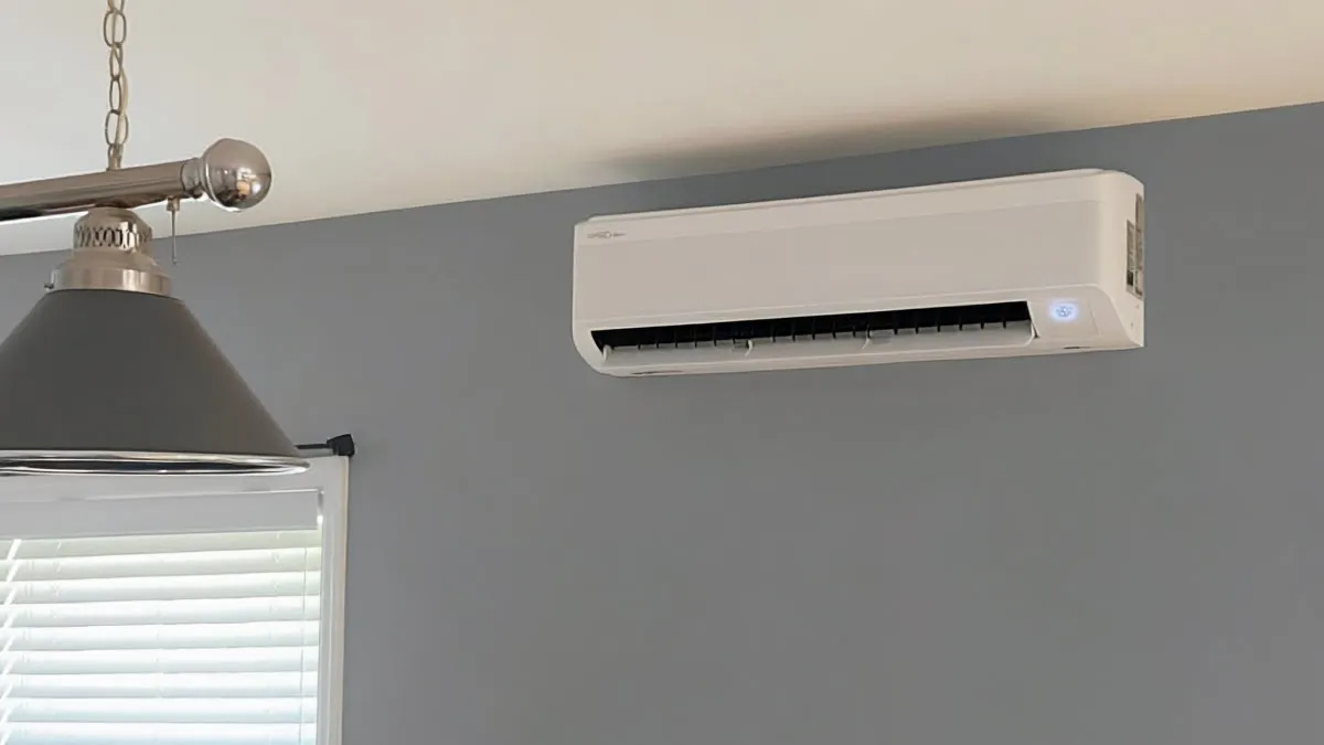 White wall-mounted air conditioner unit above window with white blinds and metal hanging light fixture.