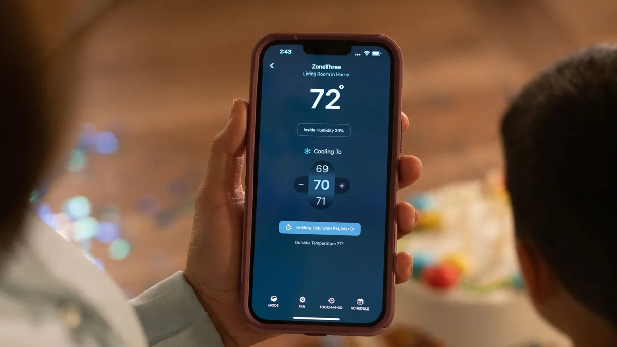 Person checking smart thermostat settings on a smartphone, displaying temperature and humidity levels.
