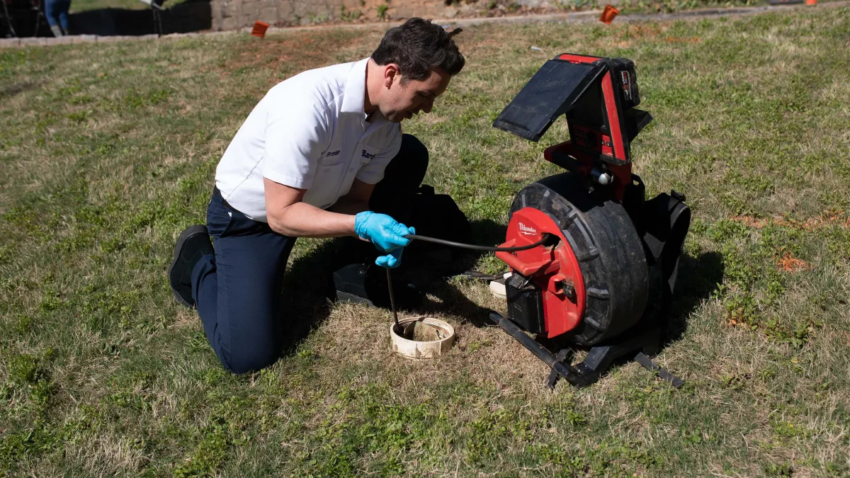 Technician using equipment to inspect sewer lines on a grassy area outdoors.