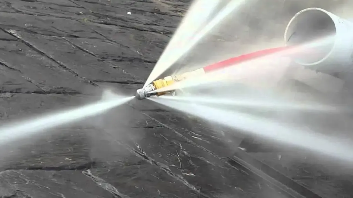 High-pressure water jet spraying from a hydrojet while exiting a pipe.