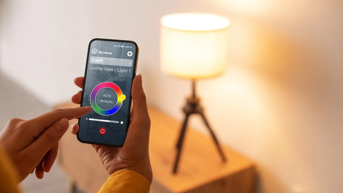 Person adjusts smart lamp brightness and color using a smartphone app in a cozy room setting.