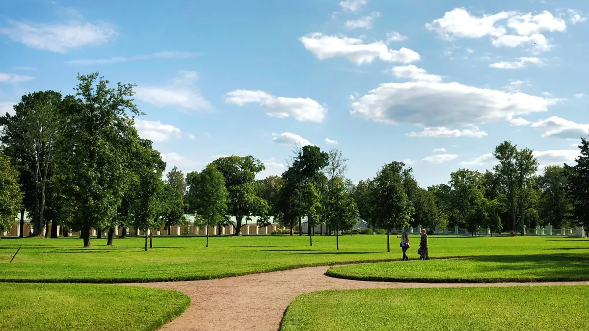 Walking path in a green park with trees, blue sky, and two people walking in the distance on a sunny day